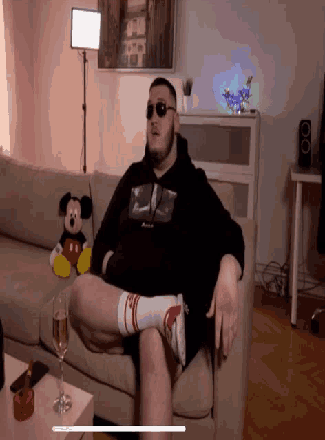 a man sits on a couch with a mickey mouse stuffed animal behind him