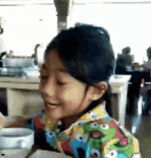 a young girl is sitting at a table with a sesame street shirt on .