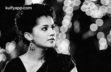a black and white photo of a woman in a saree looking at the camera .