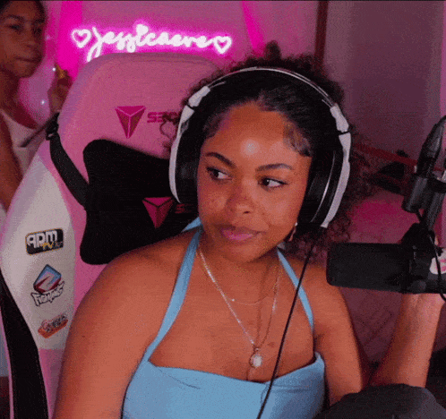 a woman wearing headphones is sitting in front of a pink chair with a neon sign that says jessleacre
