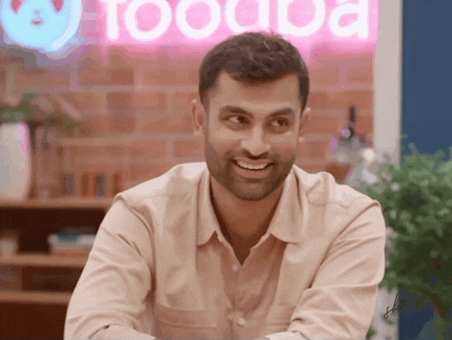 a man smiles in front of a sign that says toooda