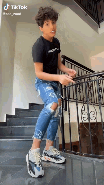 a young man is standing on a set of stairs wearing ripped jeans and sneakers .