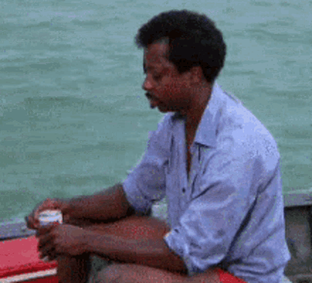 a man in a blue shirt is sitting on a boat looking at something