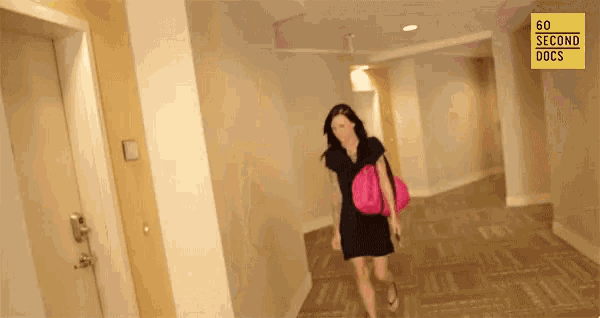 a woman in a black dress is walking down a hallway with 60 second docs on the bottom