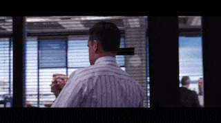 a man in a striped shirt is standing in front of a window with blinds