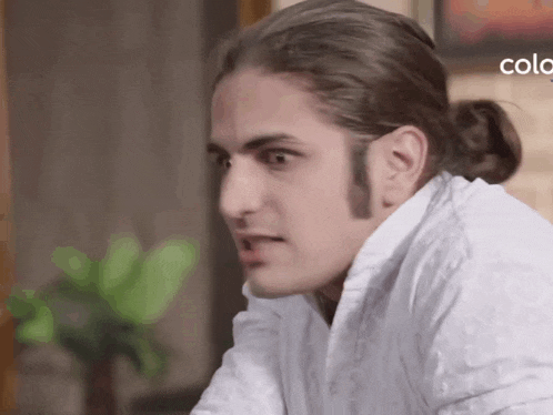 a man with long hair is wearing a white shirt and a bun .