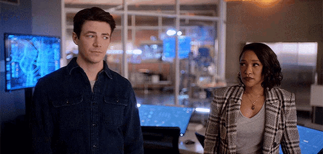 a man and a woman are standing next to each other in a room . the woman is wearing a plaid jacket .