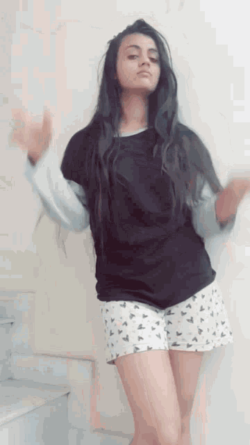 a woman in a black shirt and white shorts is dancing in front of a white wall