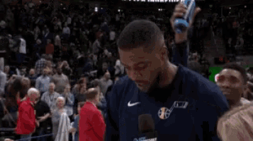 a basketball player is holding a microphone in front of a crowd of people .