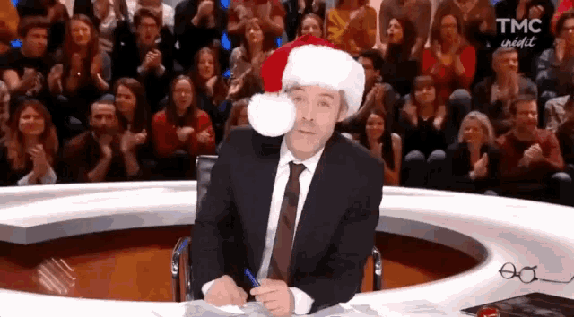 a man wearing a santa hat is sitting in front of a crowd of people