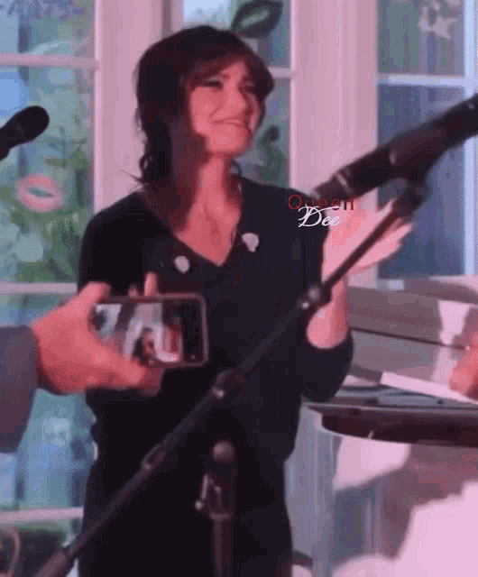 a woman stands in front of a microphone with the word dee on the bottom right