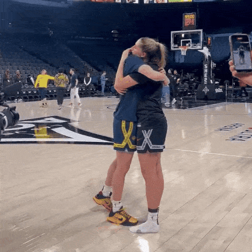 two women hugging each other on a basketball court with a scoreboard that says 10:08