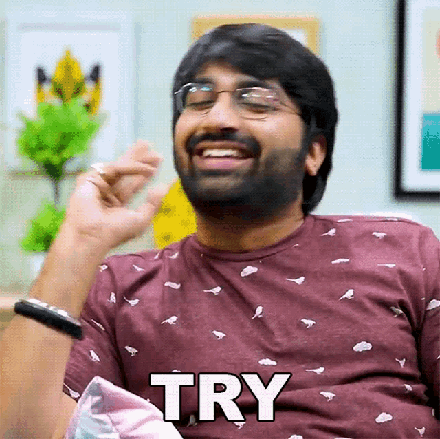 a man wearing glasses and a maroon shirt is smiling and says try