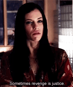 a woman with long black hair is standing in front of a window and says sometimes revenge is justice .