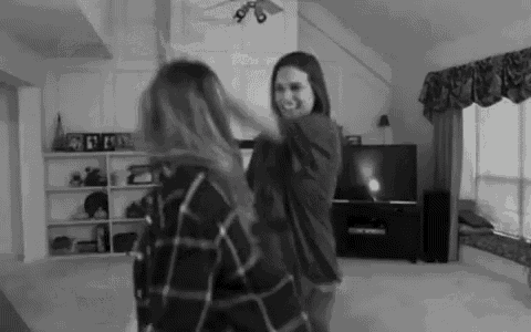 two women are dancing in a living room in front of a flat screen tv .
