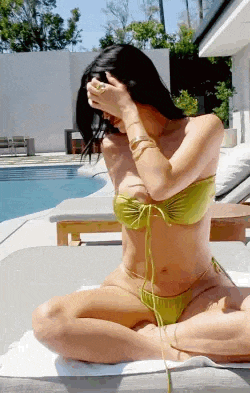 a woman in a bikini is sitting on a couch next to a pool covering her face .