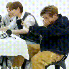 a group of people are sitting at a table with one man covering his mouth .