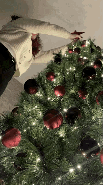 a woman is decorating a christmas tree with red and black ornaments