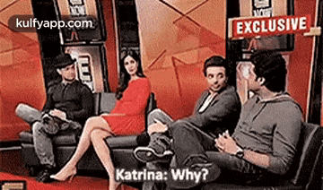 a woman in a red dress is sitting on a couch talking to two men .