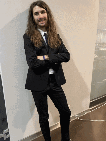 a man with long hair wearing a black suit and tie