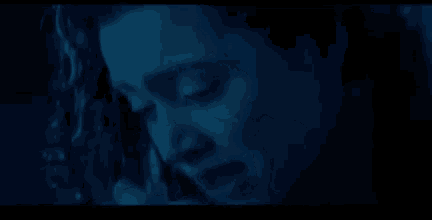 a close up of a person 's face in a dark room with a blue background .