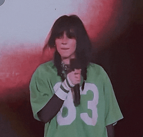 a woman in a green shirt with the number 83 on it is holding a microphone .