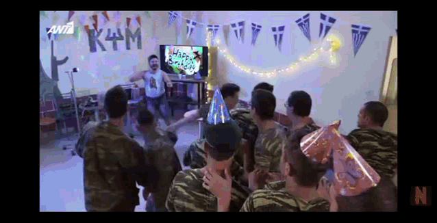 a group of soldiers are celebrating a birthday with a tv in the background that says " happy birthday "