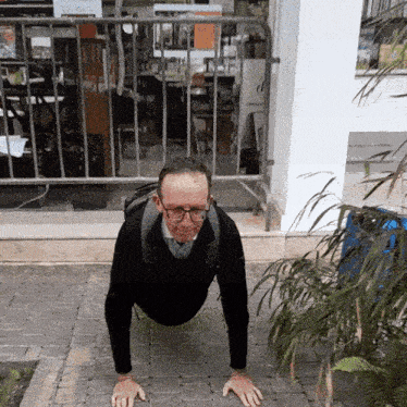 a man wearing glasses is doing push ups on a brick sidewalk