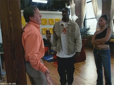 a man in an orange shirt is standing next to a man in a tan jacket and a woman in a black top ..