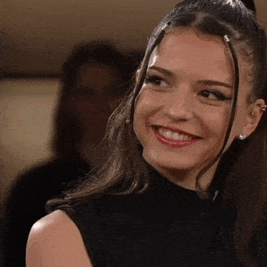 a woman wearing a black turtleneck and earrings smiles for the camera