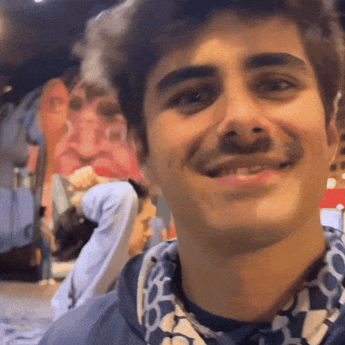 a man with a mustache is smiling and wearing a blue and white shirt