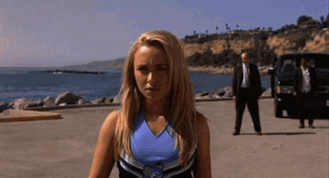 a woman in a cheerleading uniform is standing in a parking lot next to a body of water .