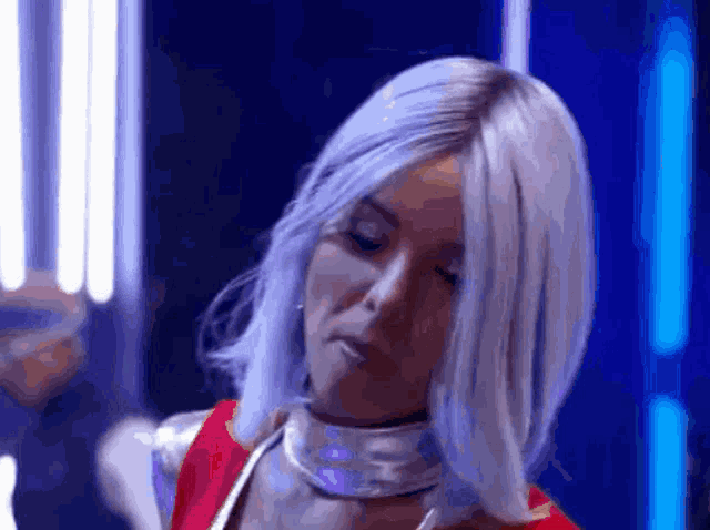 a woman with white hair is wearing a silver choker and a red dress .