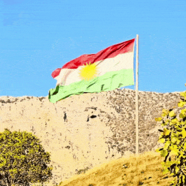 a kurdish flag is flying in the wind on top of a mountain