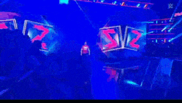 a man in a red shirt is walking on a stage with a large screen behind him that says ' mayn '
