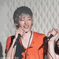a young man in an orange shirt is singing into a microphone .
