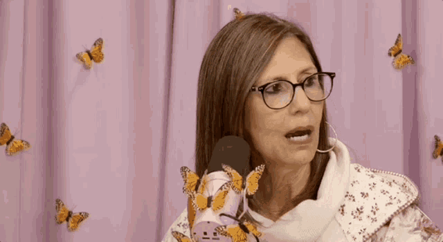 a woman wearing glasses is sitting in front of a pink microphone with butterflies flying around her .