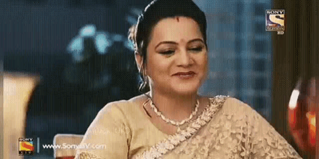 a woman in a saree is sitting at a table with a sony logo on the bottom right corner .