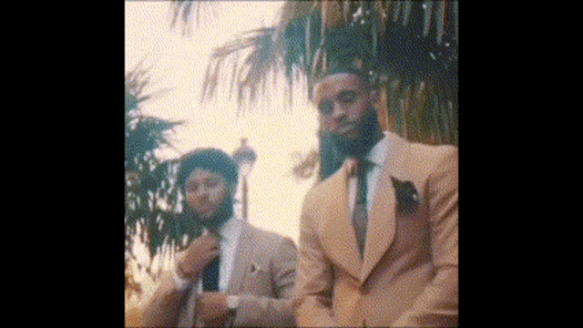 two men in suits are standing next to each other in front of palm trees .