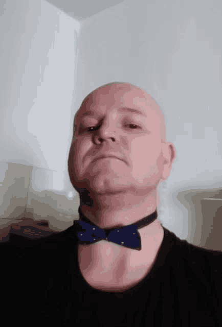 a man wearing a choker and a blue bow tie looks at the camera