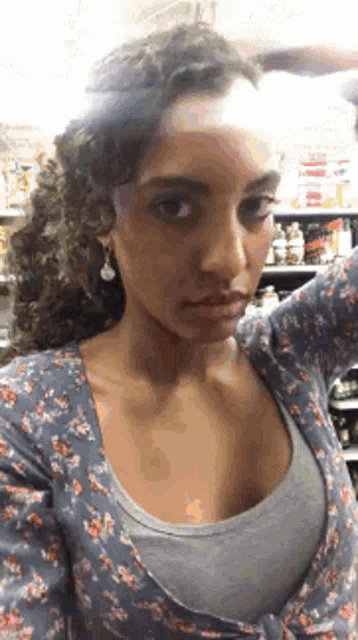 a woman with curly hair is taking a selfie with her hand on her head .