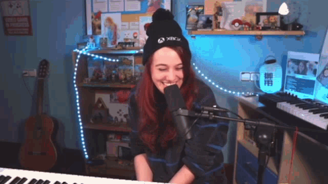 a woman singing into a microphone wearing a black xbox hat