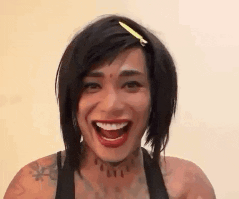 a woman with short hair and a tattoo on her neck is laughing with her mouth open .