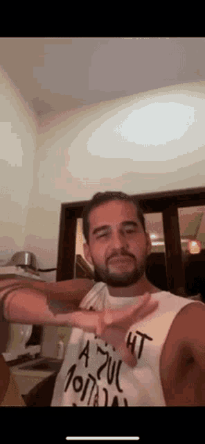 a man with a beard wearing a white tank top that says a zuc