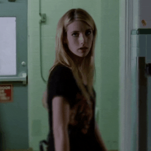 a woman in a black shirt is standing in front of a door that has a sign on it that says exit