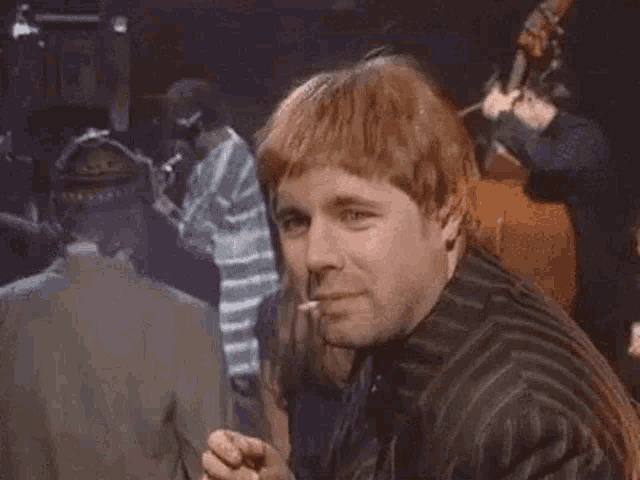 a man with red hair is giving a thumbs up sign in a crowded room .