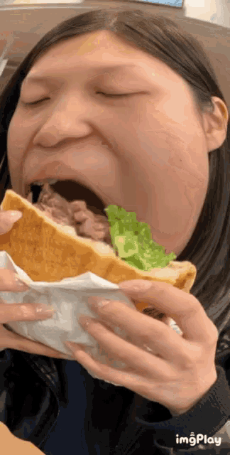 a woman is eating a sandwich with her eyes closed and the word imgplay below her