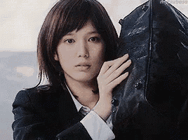 a woman in a suit is holding a black bag over her shoulder .
