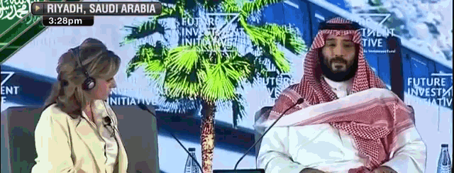 a man and a woman are sitting in front of microphones in front of a sign that says riyadh saudi arabia