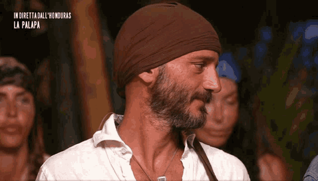 a man with a beard wears a brown headband and a white shirt